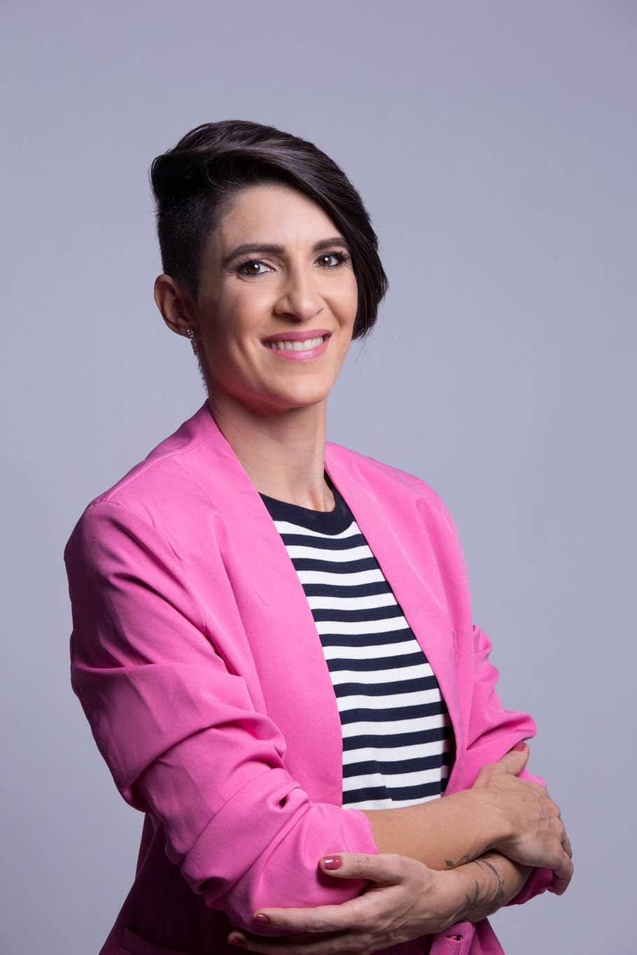 Larissa Zorzenon sorrindo, de blazer rosa e braços cruzados